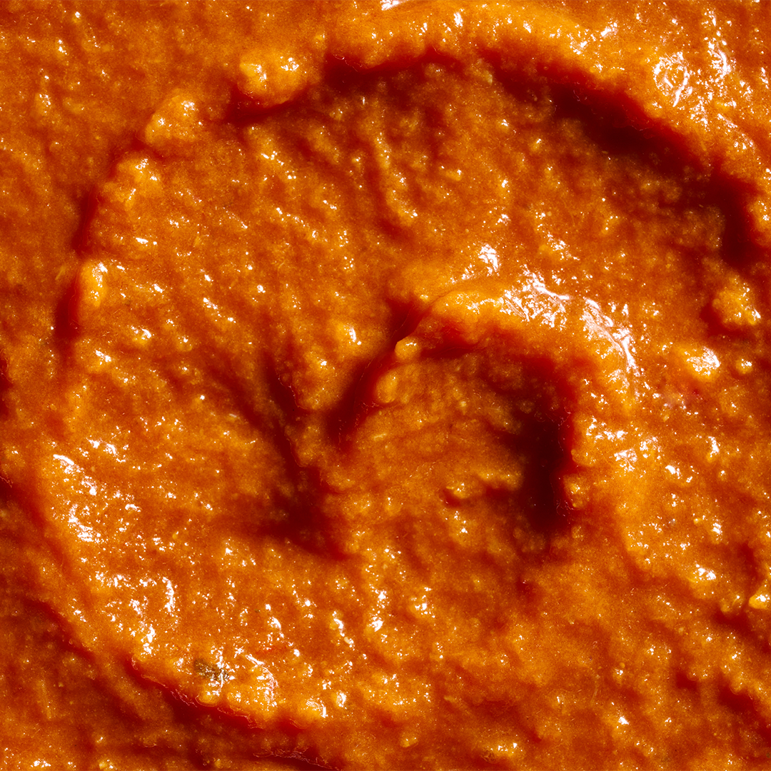 A close-up view of rich, creamy pasta sauce with a smooth, velvety texture and a vibrant orange-red hue