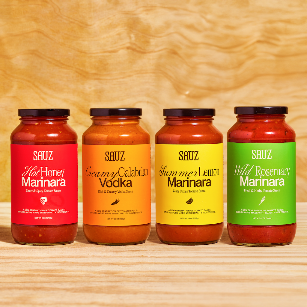 A lineup of Sauz's four sauce flavors—Hot Honey Marinara, Creamy Calabrian Vodka, Summer Lemon Marinara, and Wild Rosemary Marinara—neatly arranged on a wooden background, showcasing their bold and vibrant labels