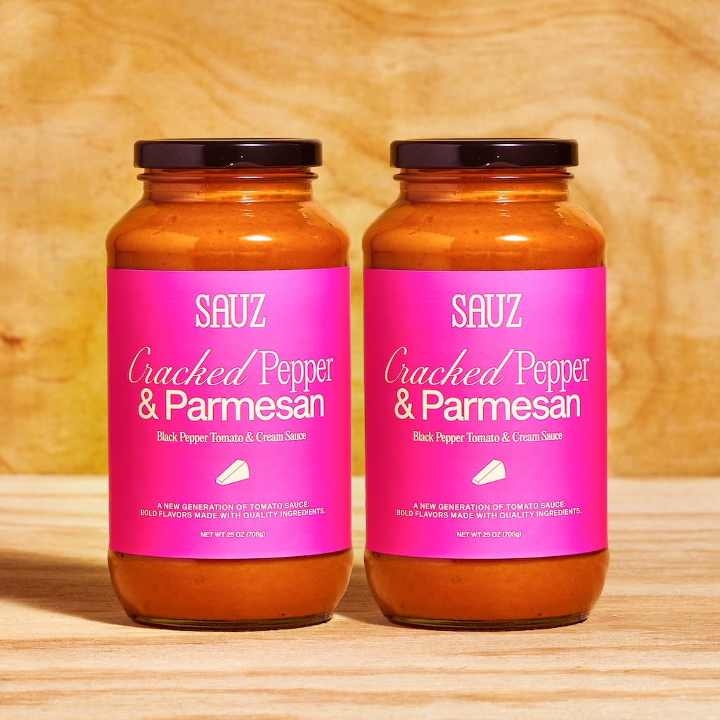 Two jars of Sauz Cracked Pepper & Parmesan sauce displayed side by side, featuring bright pink labels and a creamy tomato-based sauce inside