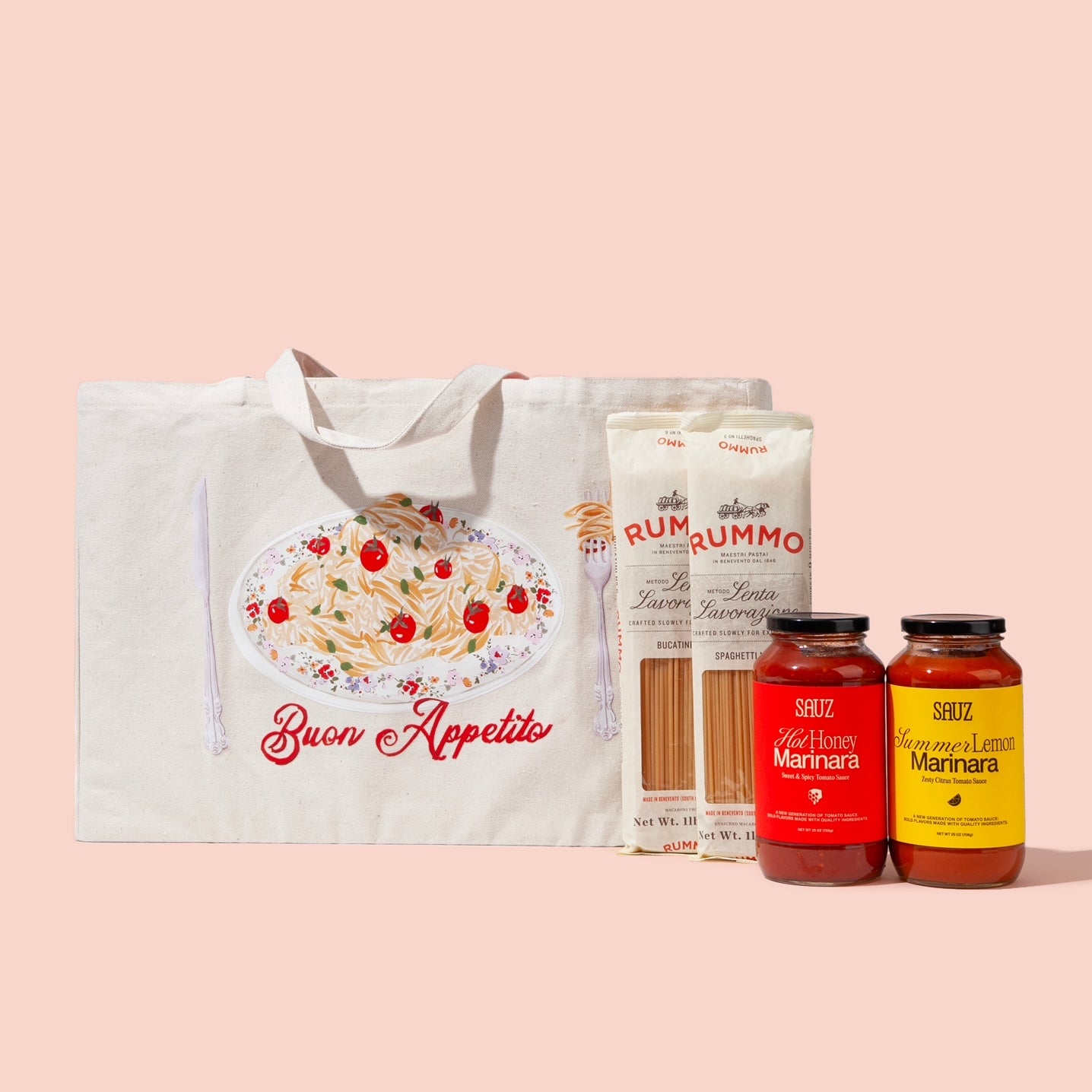 A holiday gift bundle featuring a reusable tote bag with an illustration of a pasta dish and the text 'Buon Appetito,' two packages of Rummo pasta (Bucatini and Spaghetti), and two jars of Sauz marinara sauces (Hot Honey Marinara and Summer Lemon Marinara), arranged against a light pink background