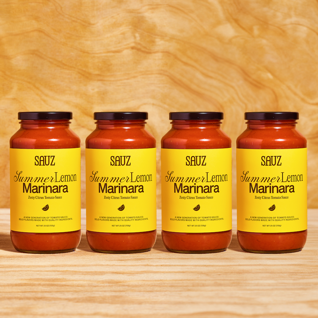 Four jars of Sauz Summer Lemon Marinara sauce arranged side by side on a wooden surface, featuring bright yellow labels that highlight the zesty citrus tomato flavor