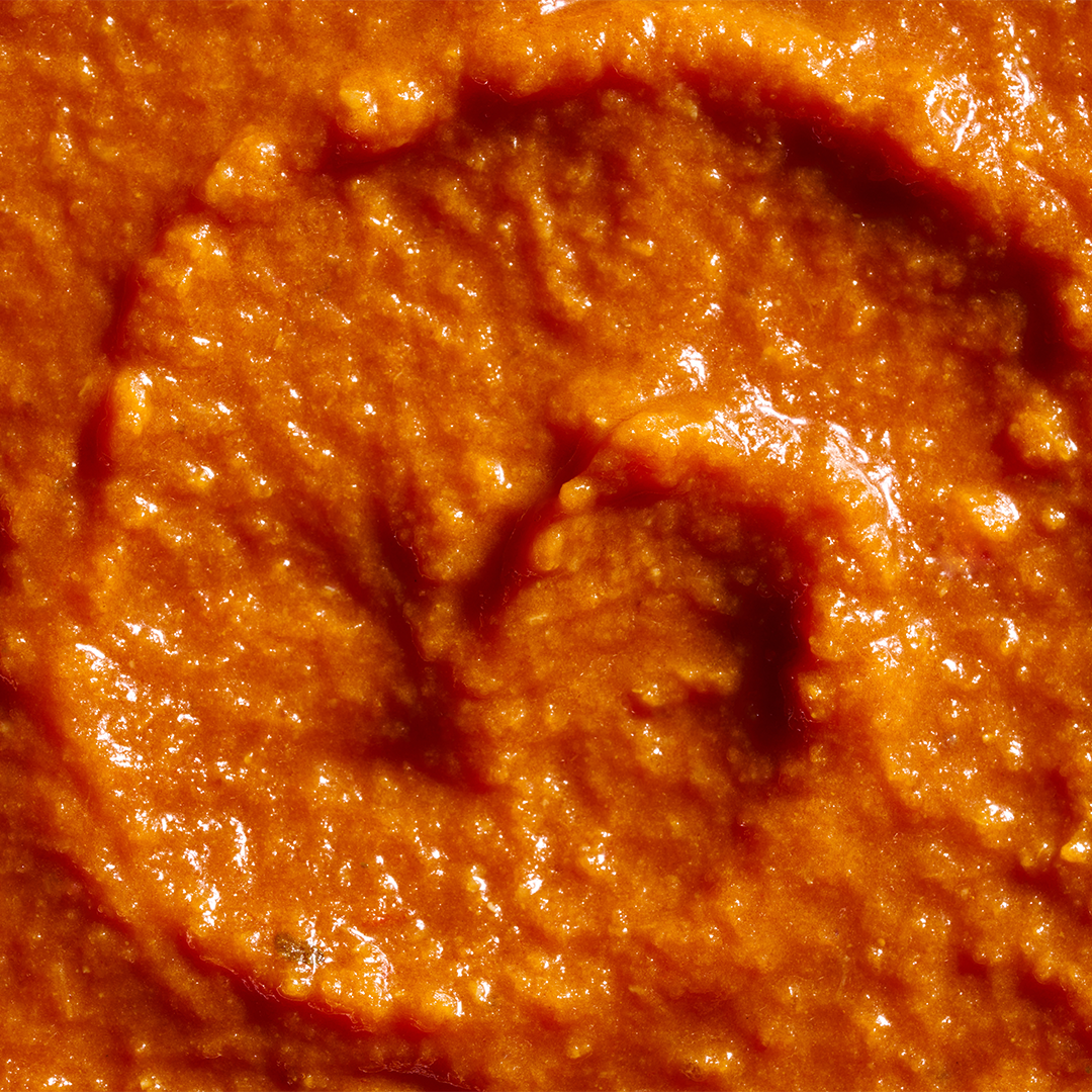 A close-up of creamy orange-red pasta sauce with a smooth yet slightly textured surface, showing swirls and glossy highlights